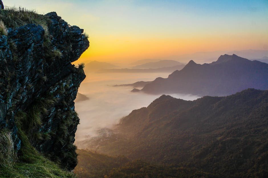 Peaceful mountain landscape at sunrise with clouds and sun backlighting the scene.