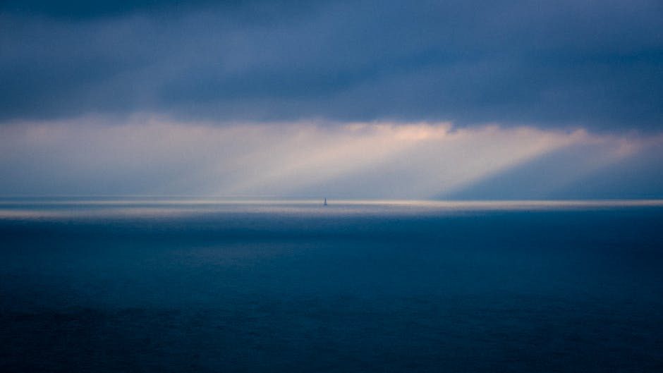 A serene ocean view at dawn with beams of light breaking through dramatic clouds.